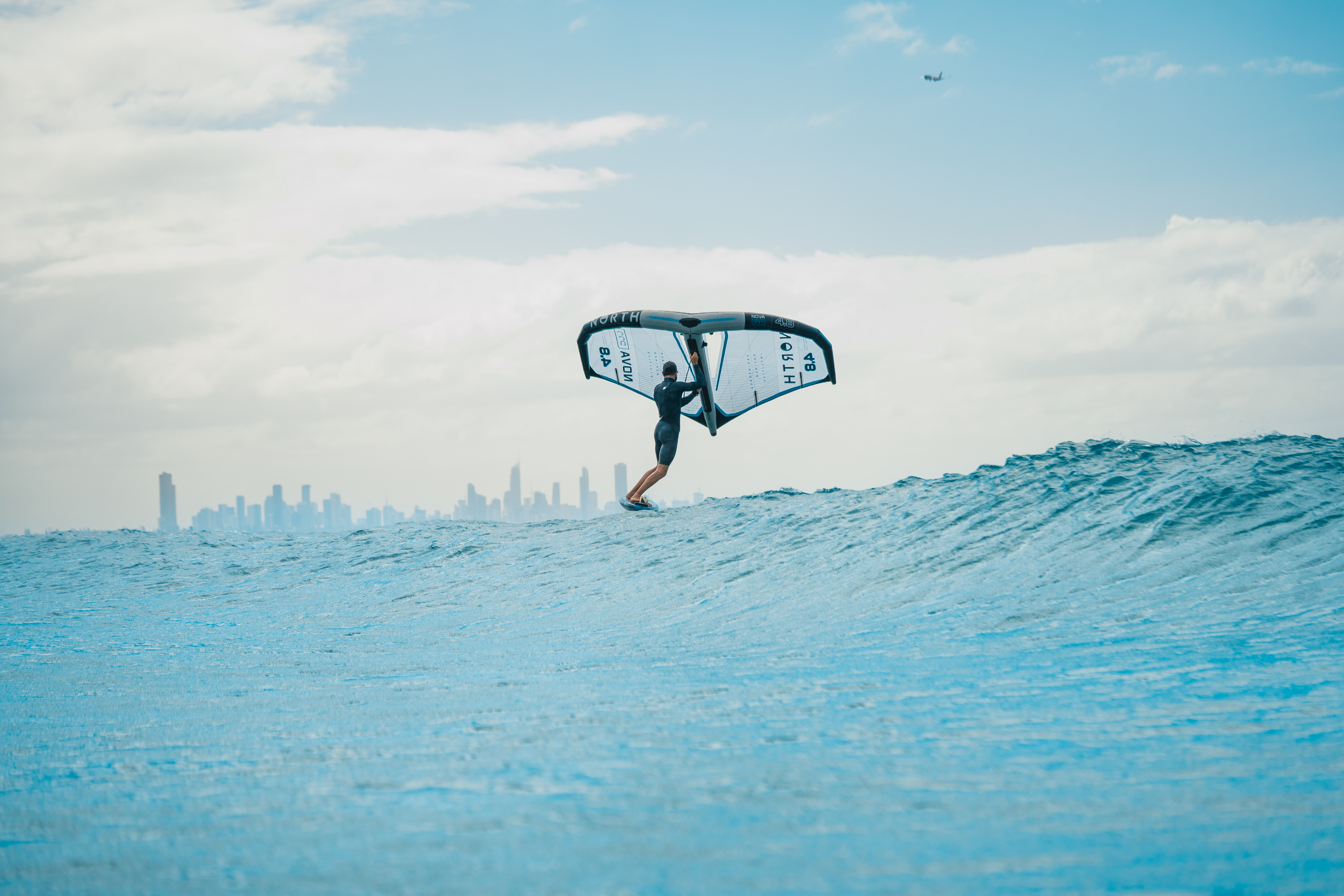 Wingfoil rider on a blue wave with skyline in the distance